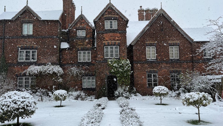 The front exterior of Moseley Old Hall with snow on the ground and roof of the building. Snow is also seen falling in the image.